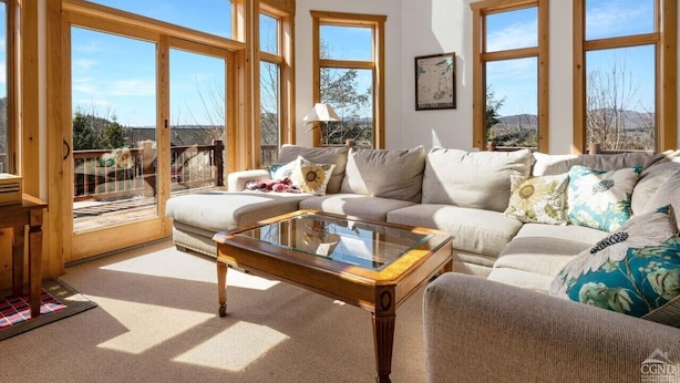 A spacious living room with large windows, a glass coffee table, and a sofa with decorative pillows. - Luxe 8BR Windham Lodge | Theater, Walk to Slopes (Windham)
