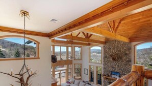 A spacious room with large windows, wooden beams, and a stone wall. - Luxe 8BR Windham Lodge | Theater, Walk to Slopes (Windham)