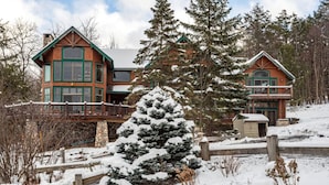 A large log cabin with a stone foundation, multiple windows, and a balcony. - Luxe 8BR Windham Lodge | Theater, Walk to Slopes (Windham)