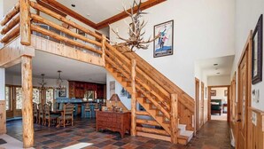 A spacious interior with a wooden staircase, a dining area, and a kitchen. - Luxe 8BR Windham Lodge | Theater, Walk to Slopes (Windham)