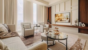 Een moderne woonkamer met een bank, fauteuils, een salontafel en een aan de muur bevestigde televisie.