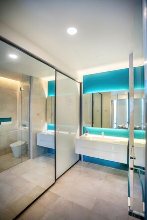 A modern bathroom with a glass shower enclosure, a white sink with a blue accent, and a large mirror. - Tropicana The Residences KLCC Skypool (Kuala Lumpur)