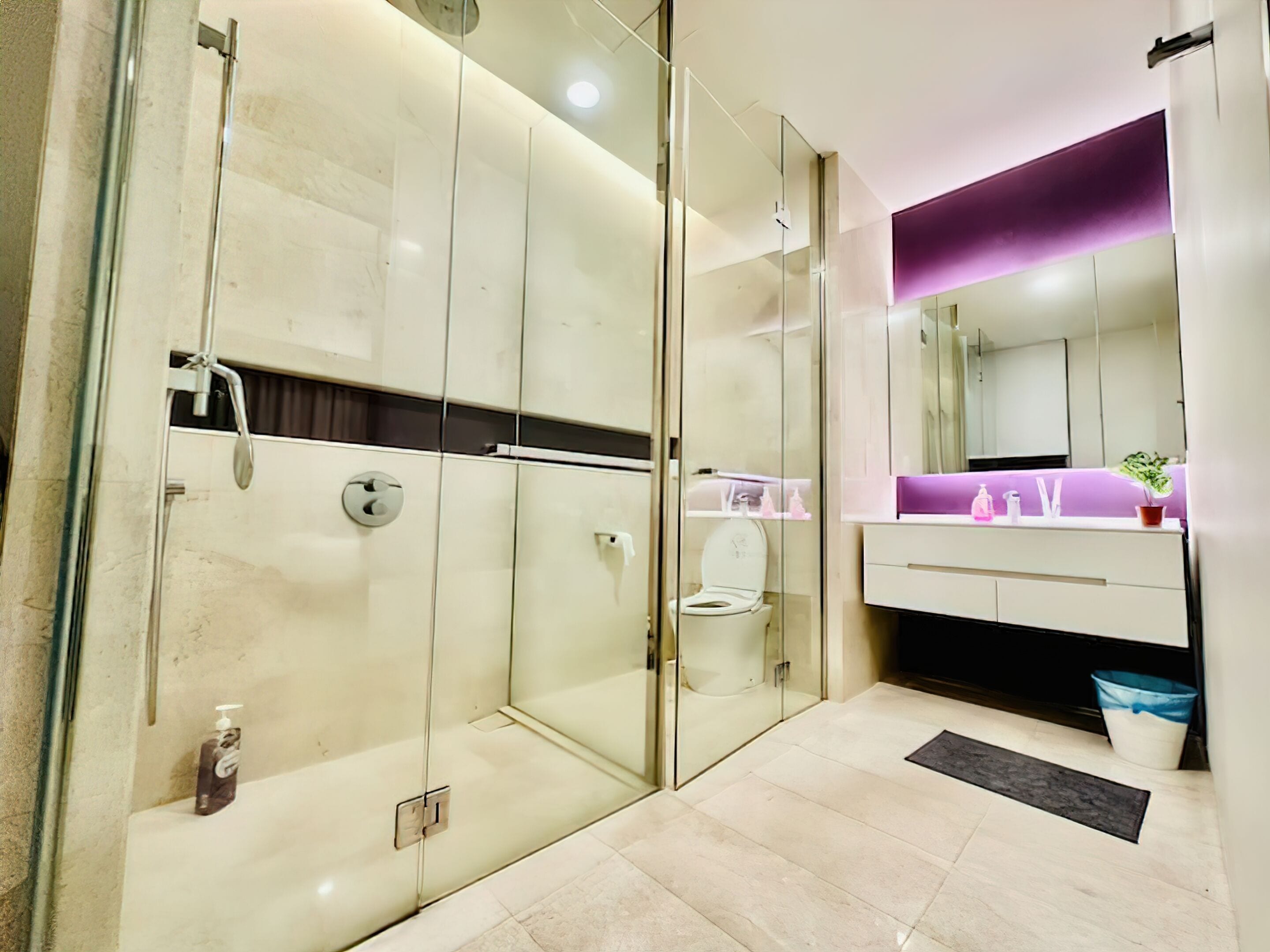 A modern bathroom with a glass-enclosed shower, a vanity with a purple accent wall, and a large mirror.