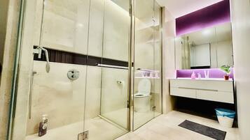 A modern bathroom with a glass-enclosed shower, a vanity with a purple accent wall, and a large mirror.