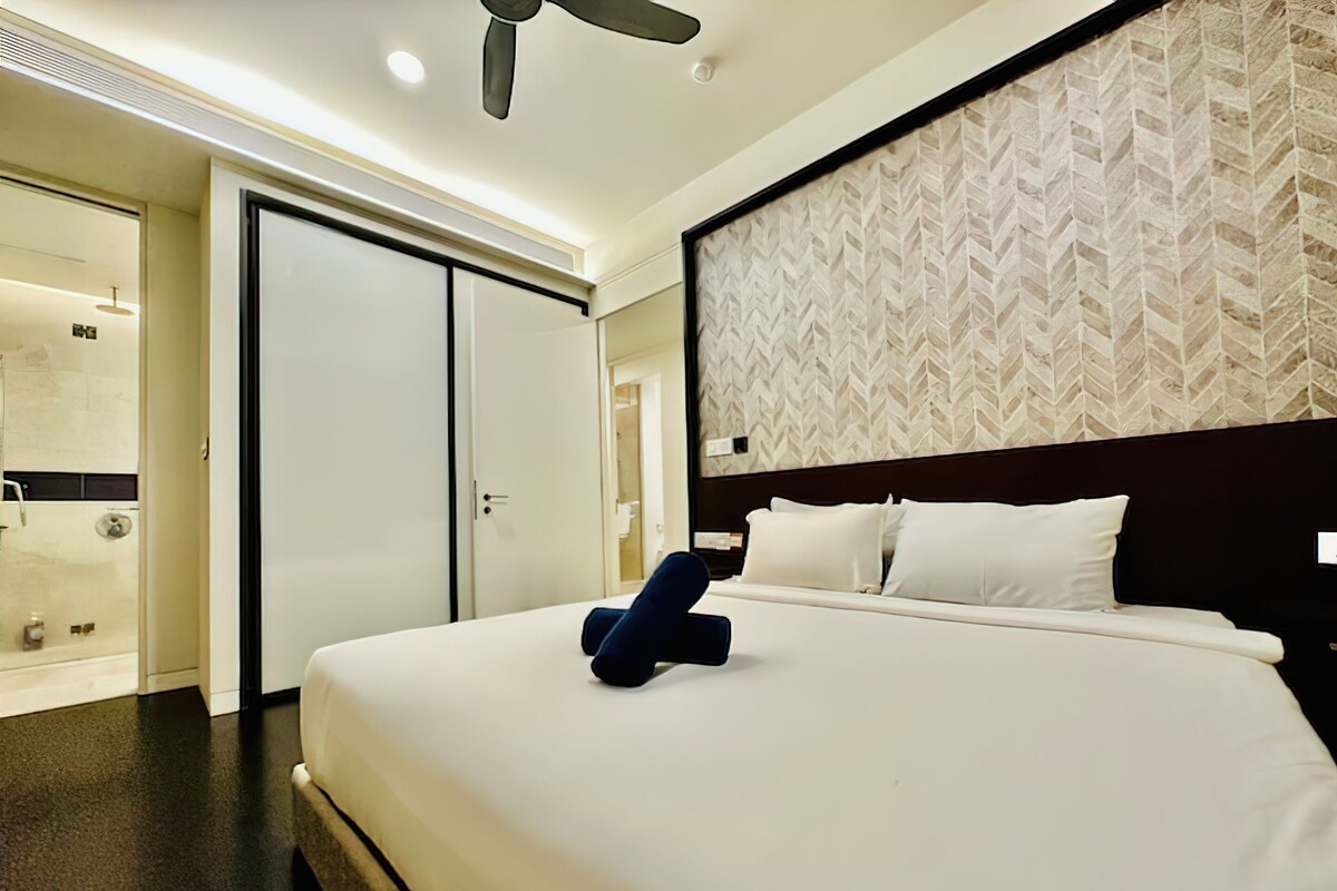 Une chambre d’hôtel avec un grand lit, une tête de lit sombre et un mur orné d’un motif.