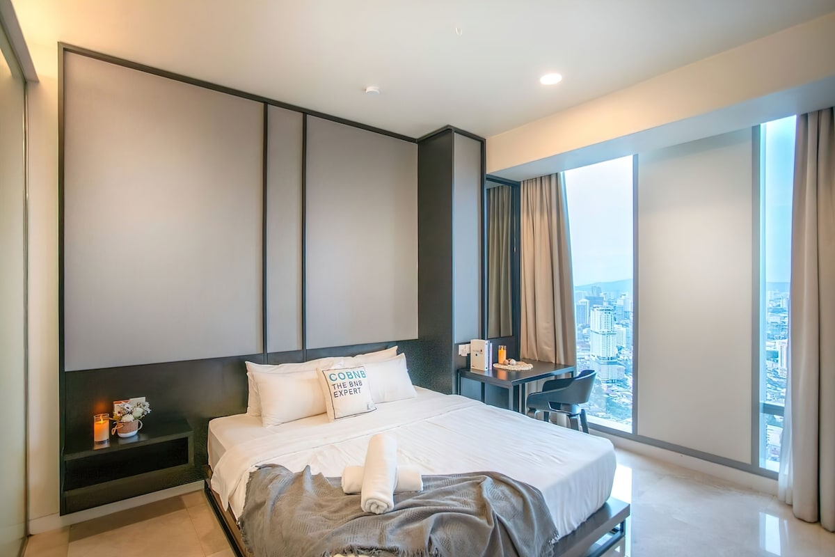 Une chambre d’hôtel moderne, dotée d’un grand lit, d’un bureau et offrant une vue sur la ville par la fenêtre.