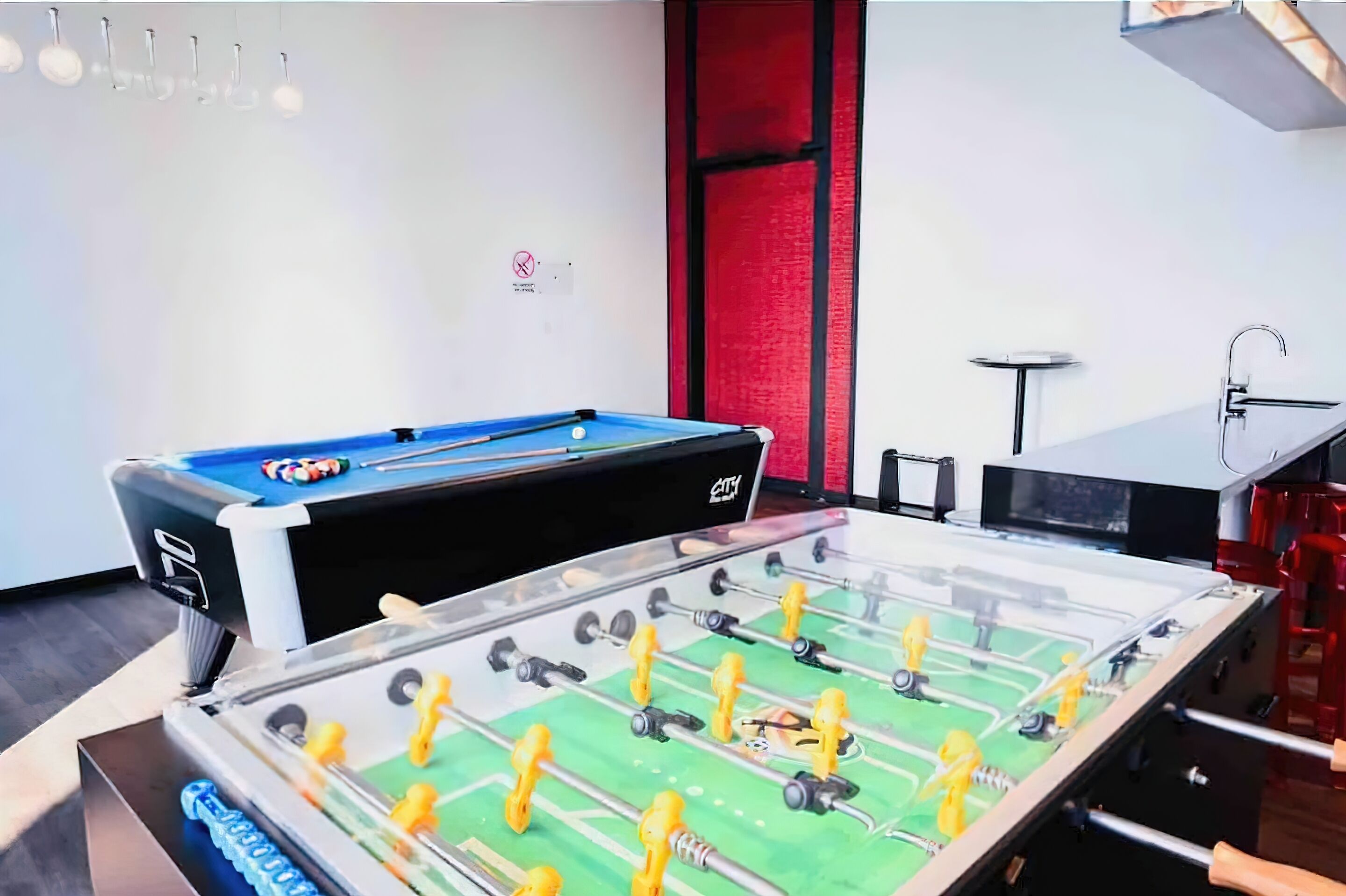 A room with a foosball table, a pool table, and a billiards table.