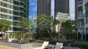 A rooftop terrace with two lounge chairs, a stone planter with flowers, and a view of surrounding high-rise buildings. - The Lofts Central, Burj khalifa View (Dubai)