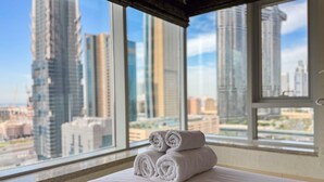 A hotel room with a bed, a window with a view of tall buildings, and a stack of rolled towels. - The Lofts Central, Burj khalifa View (Dubai)