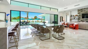 A modern interior with a large dining area, a pool view, and a cozy seating area. - Pool + Hot Tub + Putting Green + Fire Pit • Near La Quinta + Golf | Bravo (Indio)