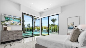 A modern bedroom with a large bed, a TV, and a view of a swimming pool.