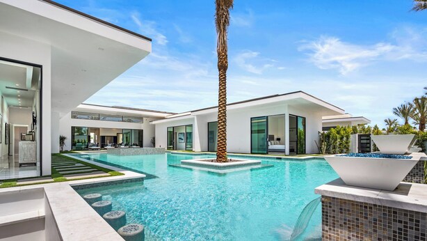 A modern house with a swimming pool, a palm tree, and a clear blue sky.