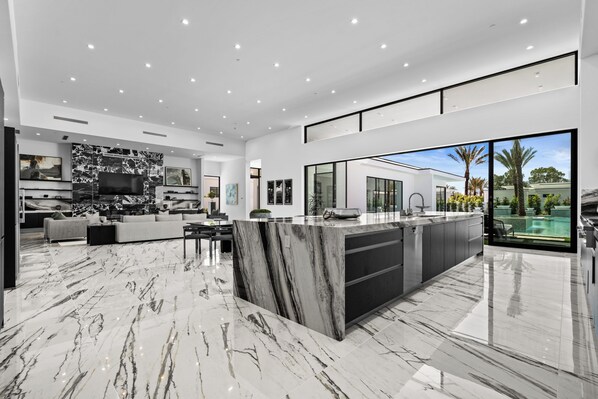 A modern kitchen with a marble countertop, a large island, and a dining area with a sofa and chairs.