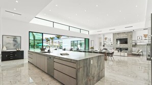 A modern kitchen with a large island, a dining area, and a living space with a TV.