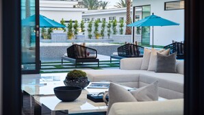 A modern living room with a sofa, a coffee table, and a view of a courtyard with outdoor furniture and umbrellas.