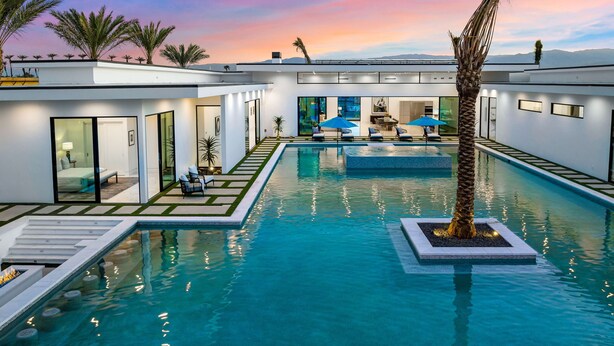 A modern pool area with a clear view of the pool, lounge chairs, and a palm tree.
