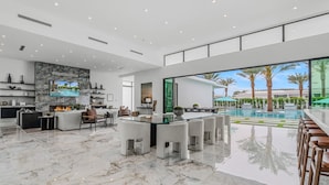 A spacious living area with a marble floor, a glass dining table, and a poolside view. - Sleeps 17 • Private Pool + Hot Tub + Pickleball Court • Near La Quinta | Bravo (Indio)