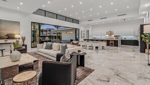 A spacious living area with a large sofa, a dining table, and a kitchen in the background. - Sleeps 17 • Private Pool + Hot Tub + Pickleball Court • Near La Quinta | Bravo (Indio)
