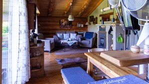Interior rústico de cabaña con vigas de madera, un sofá, una mesa de comedor y un escurridor de cocina colgante.