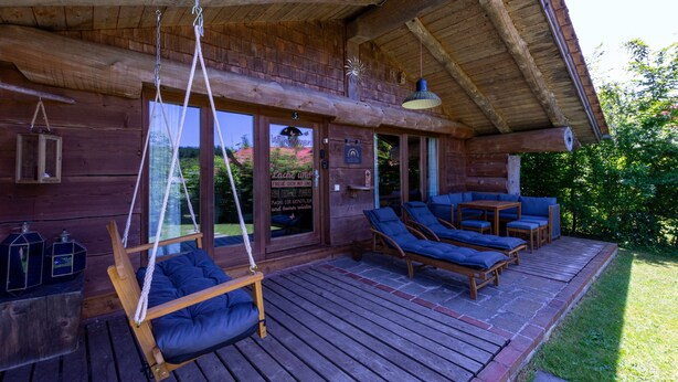 Una cabaña de madera con porche, mobiliario exterior y una mecedora.