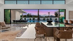 Un intérieur moderne avec un bar, des espaces pour s’asseoir et une vue sur la piscine.