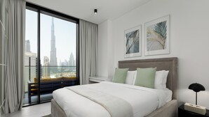 A modern hotel room with a large bed, a nightstand, a view of the city skyline, and two framed artworks on the wall. - Maison Privee - Sky-High Panoramic Apt with Iconic Burj Khalifa Views (Dubai)