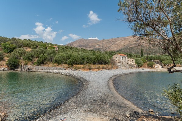 A clear view of a pebble beach leading to a calm lake, surrounded by hills and sparse vegetation.