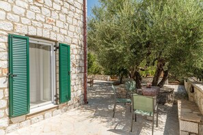 A stone building with green shutters, outdoor seating, and an olive tree.