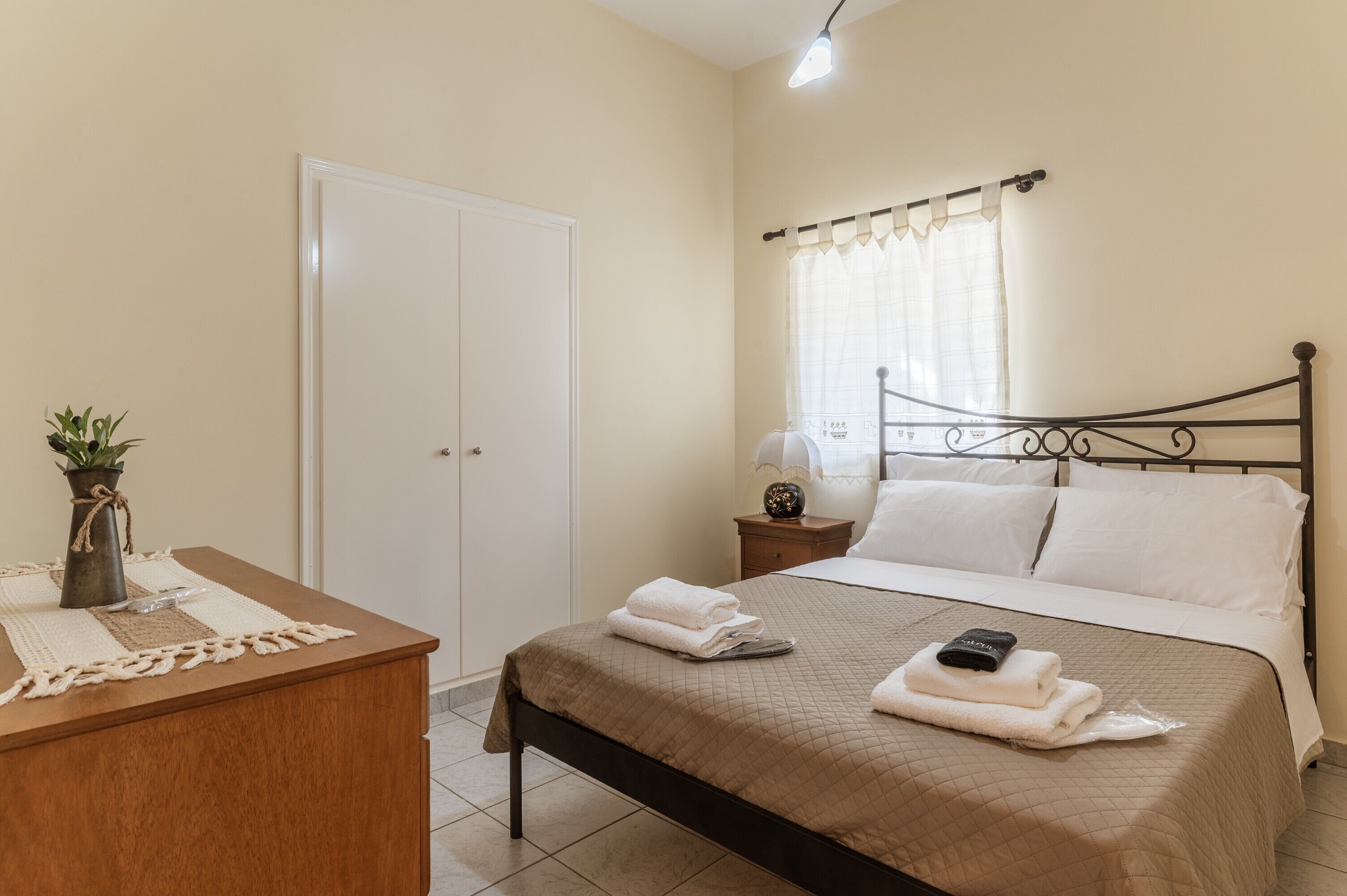 Quarto com cama, mesa de cabeceira, luminária, planta em vaso e guarda-roupa.
