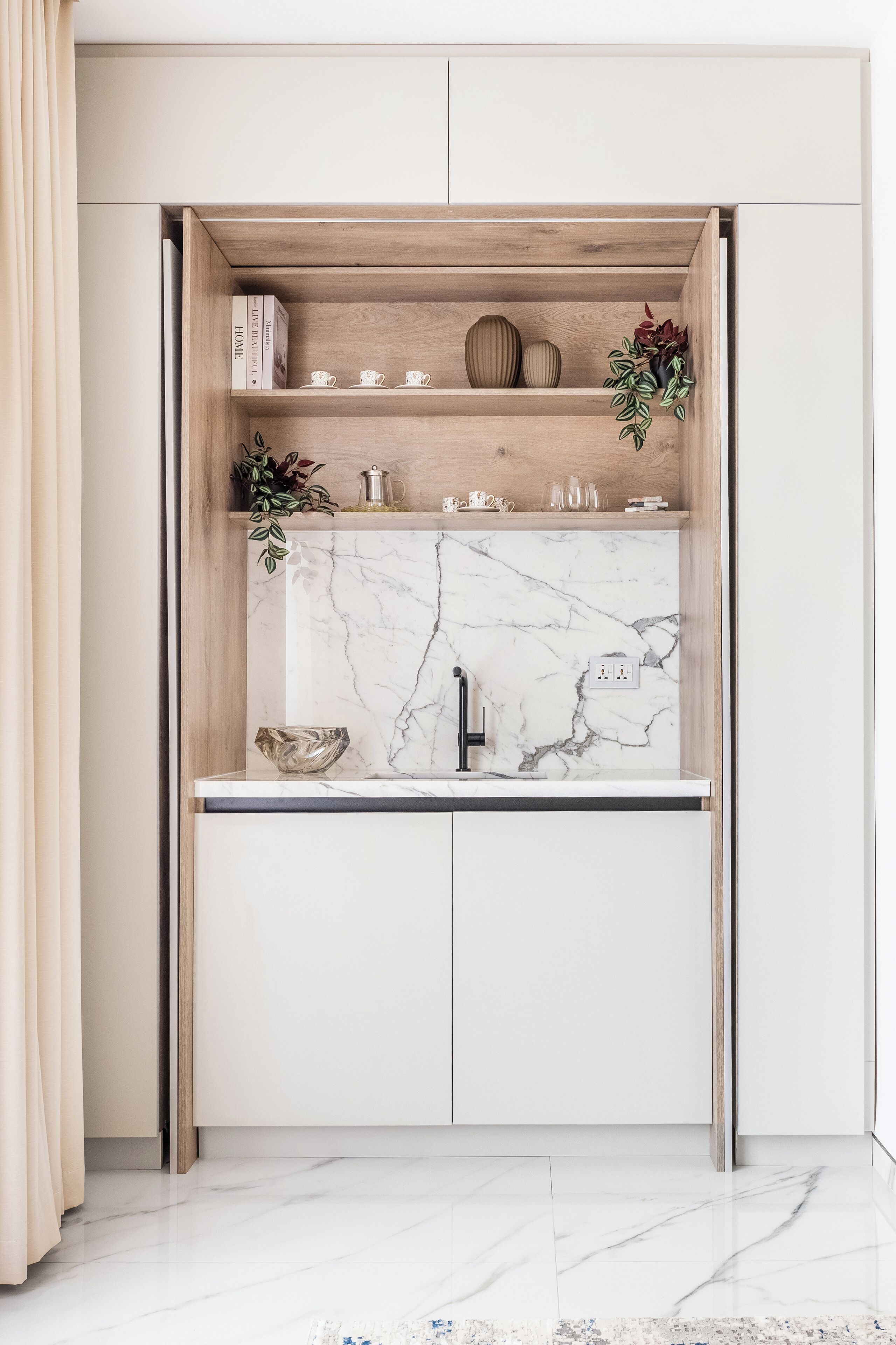 A compact kitchen with a marble countertop, a sink, and a built-in shelf with decorative items.