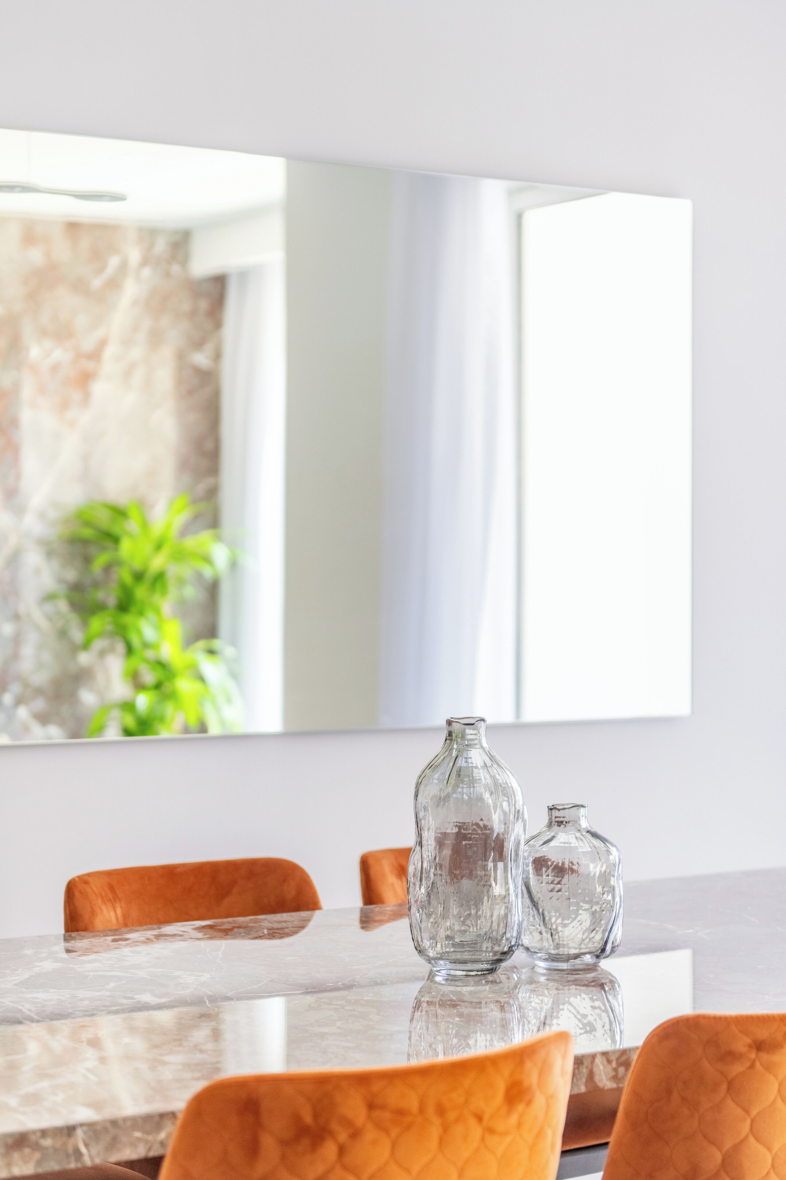 A dining area with a marble table, orange chairs, and two clear glass vases.