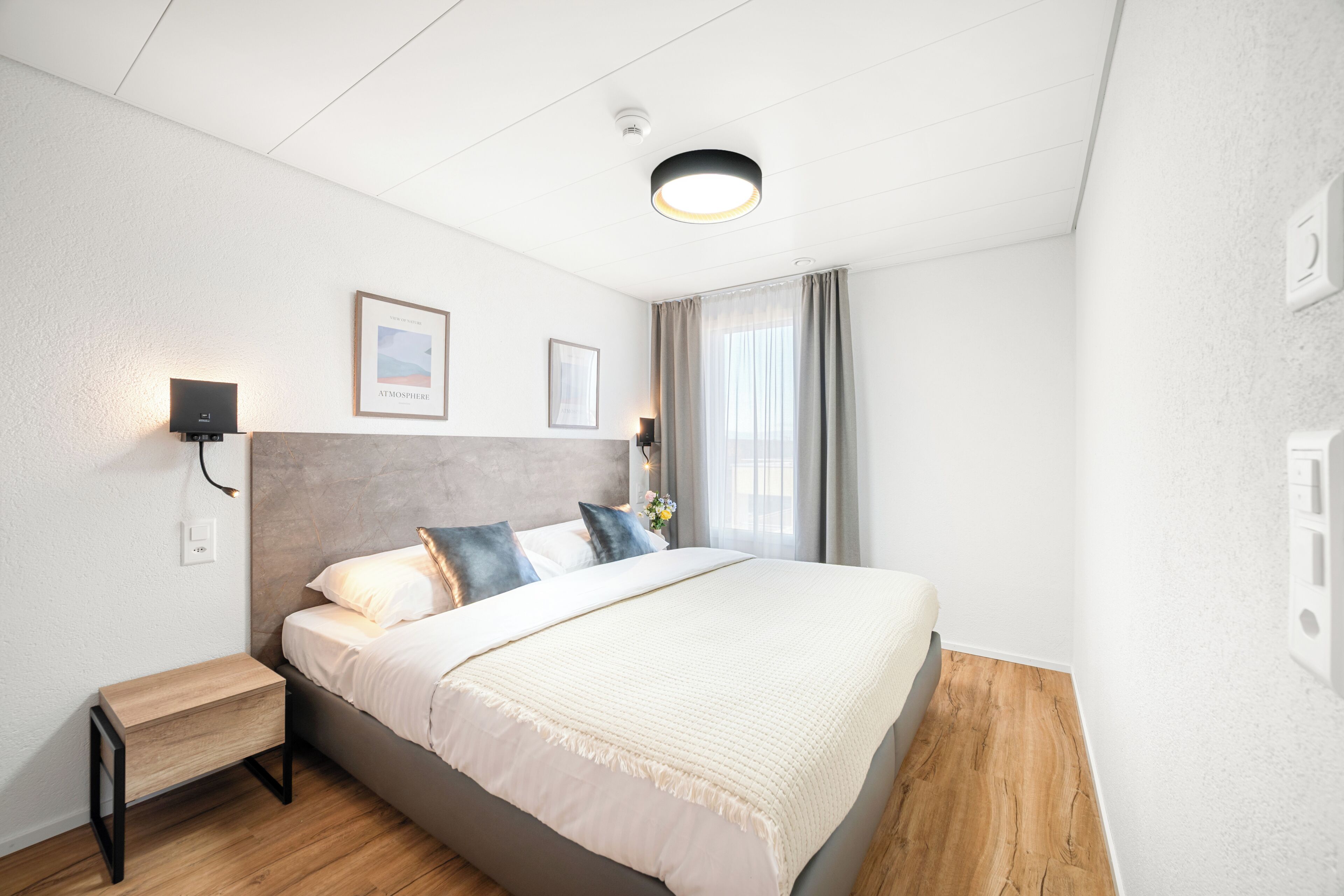 Un dormitorio moderno con una cama grande, una mesita de noche, una lámpara de pared y una luz en el techo.