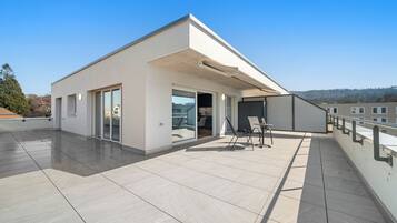 A modern building with a flat roof, large sliding glass doors, and a patio area with a table and chairs.
