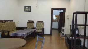 A living room with a sofa set, a dining table with chairs, a small kitchen area with a shelf, and a doorway leading to another room. - ALI XAYATHIT APARTMENT & HOTEL (Vientiane)