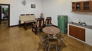 A compact kitchen with a dining area, a green refrigerator, wooden cabinets, and a ceiling fan. - ALI XAYATHIT APARTMENT & HOTEL (Vientiane)