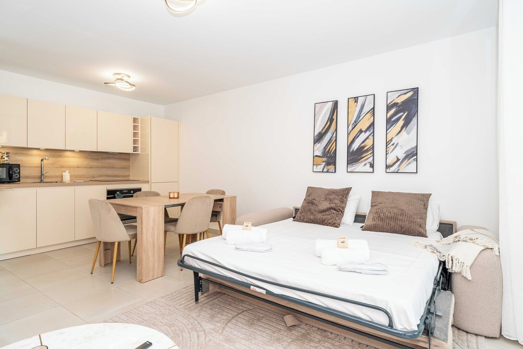 A modern hotel room with a bed, a desk, and a kitchenette.