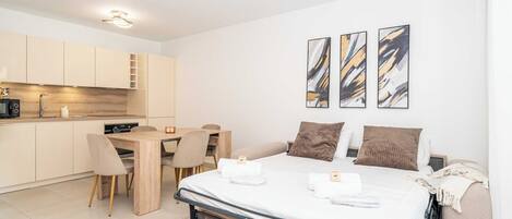A modern hotel room with a bed, a desk, and a kitchenette.