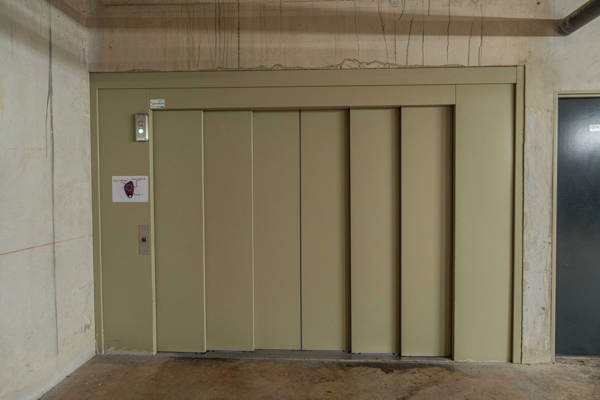 Puerta cerrada de un ascensor con un panel de control y un cartel que indica su ubicación.