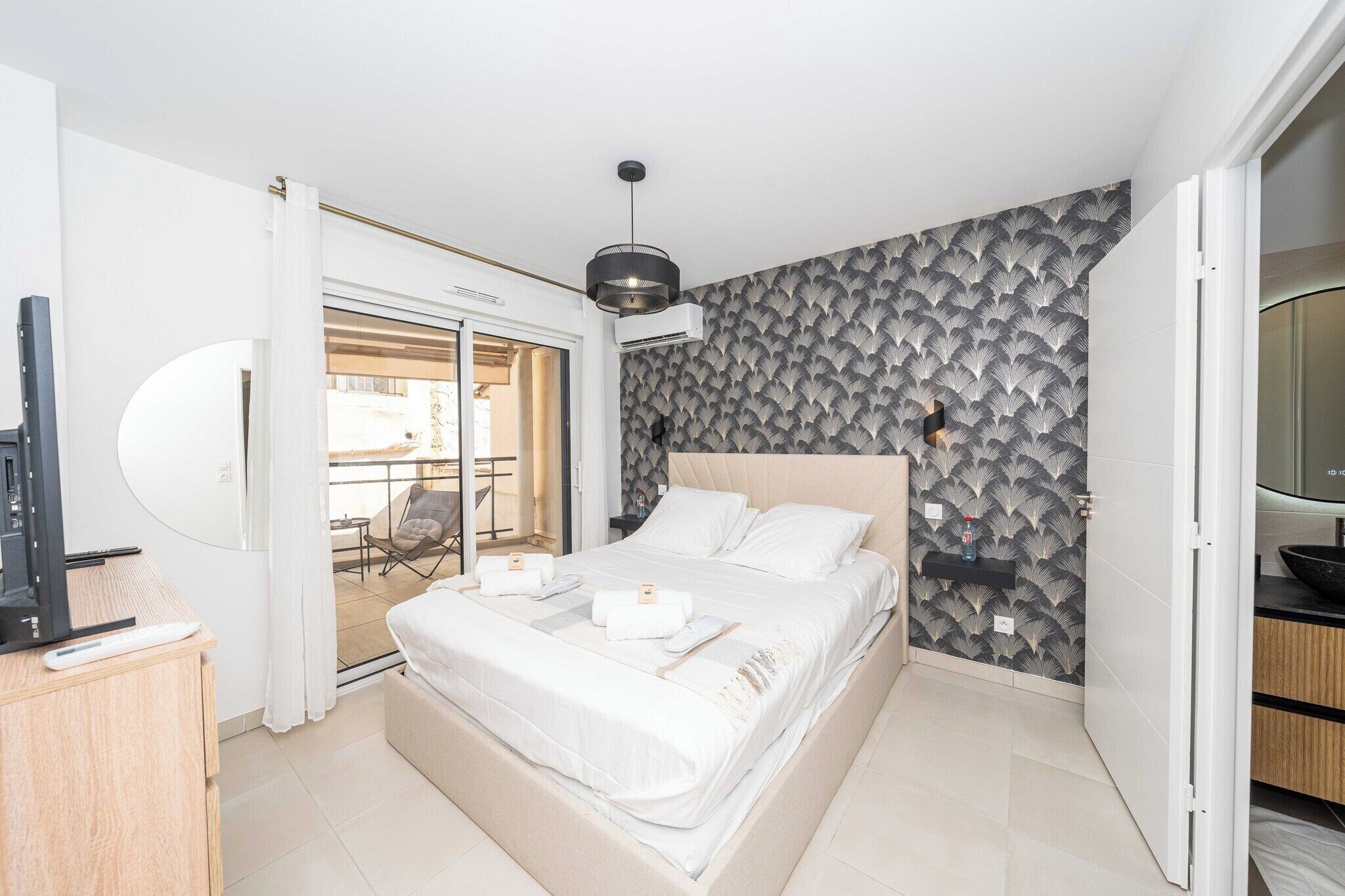 Une chambre d’hôtel moderne équipée d’un lit, d’une télévision, d’un bureau et d’un balcon avec une chaise.