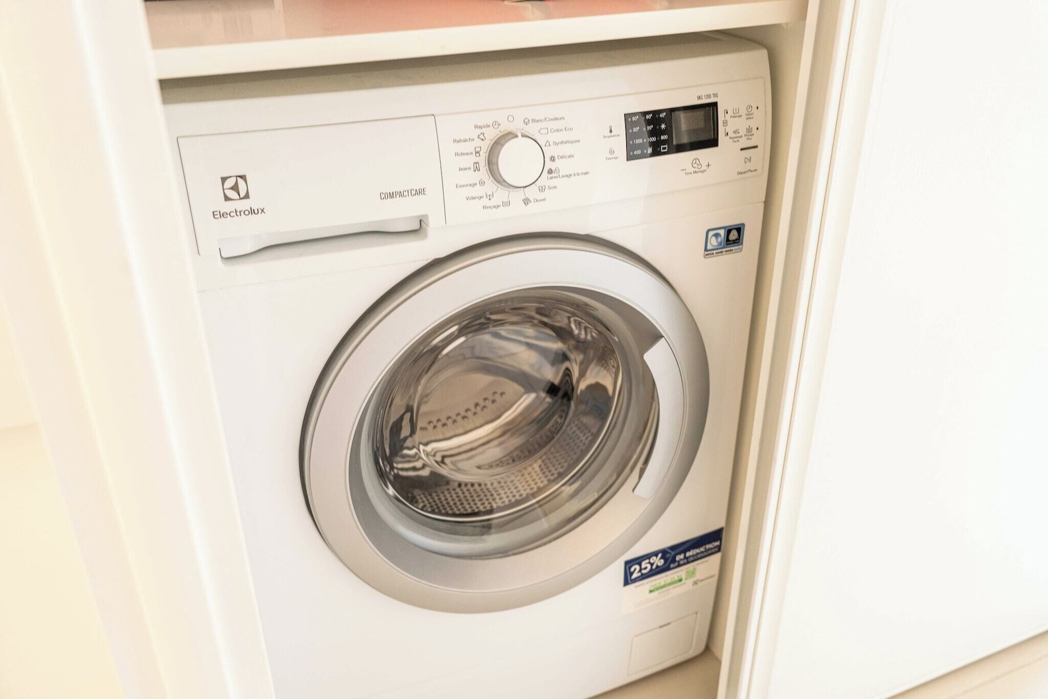 Vue de face d’un lave-linge compact doté d’un panneau de commande numérique et d’une porte transparente.