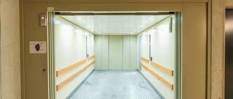 Un ascenseur doté d’un plancher métallique et de murs de couleur beige, avec un panneau de commande et un bouton d’arrêt d’urgence situés sur le côté gauche.