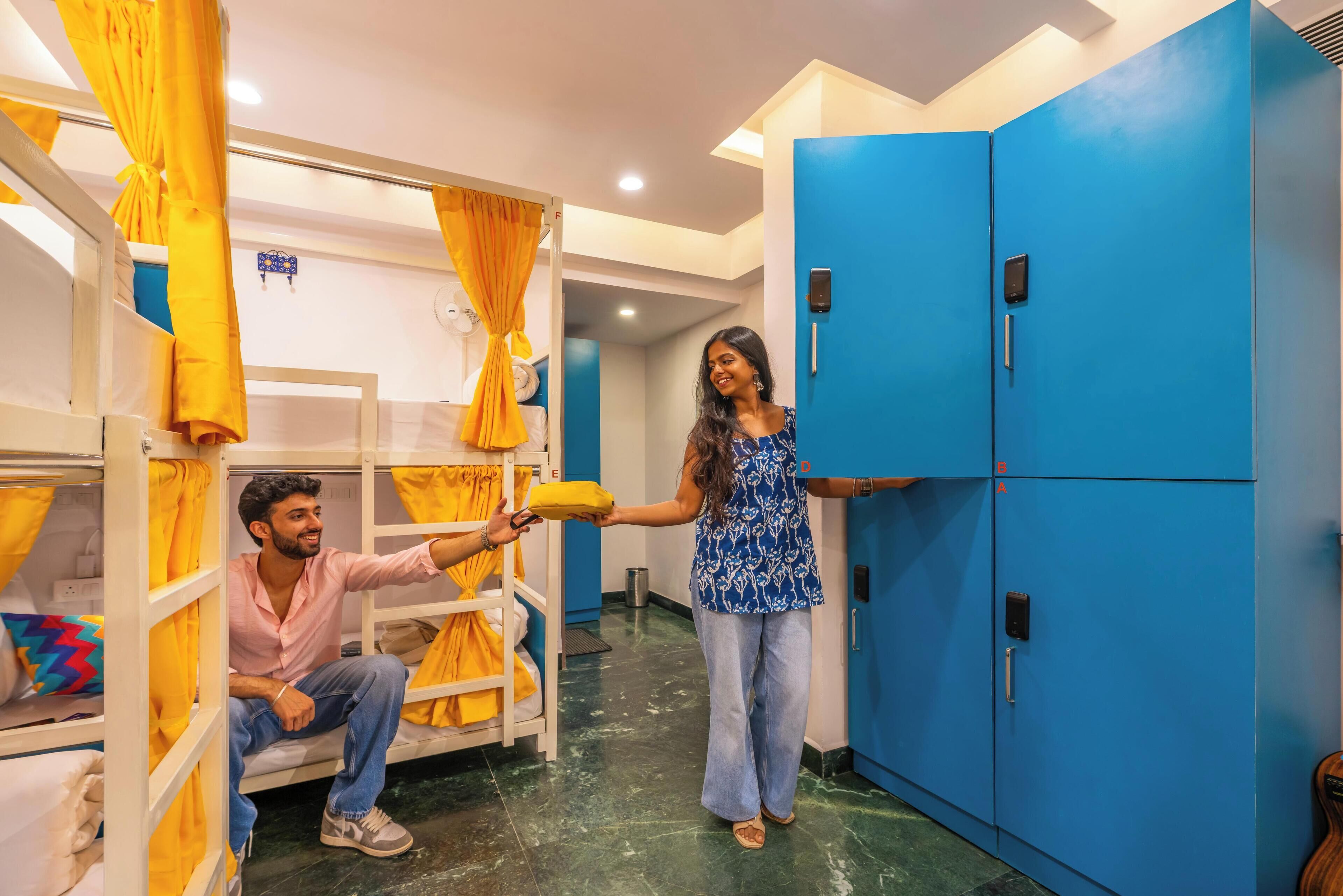 A hotel room with bunk beds, a blue wardrobe, and a person handing over a pillow.