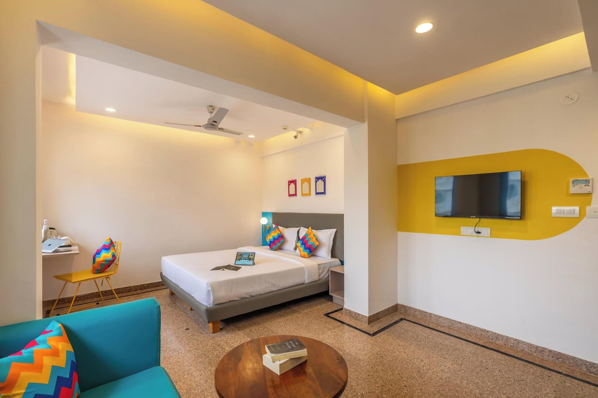 A hotel room with a bed, a desk, a chair, a TV, and a coffee table.