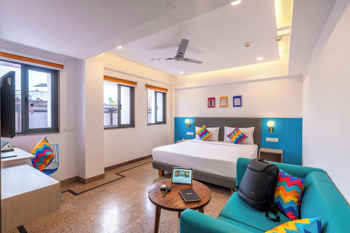 A hotel room with a bed, a desk, a chair, a sofa, and a ceiling fan.