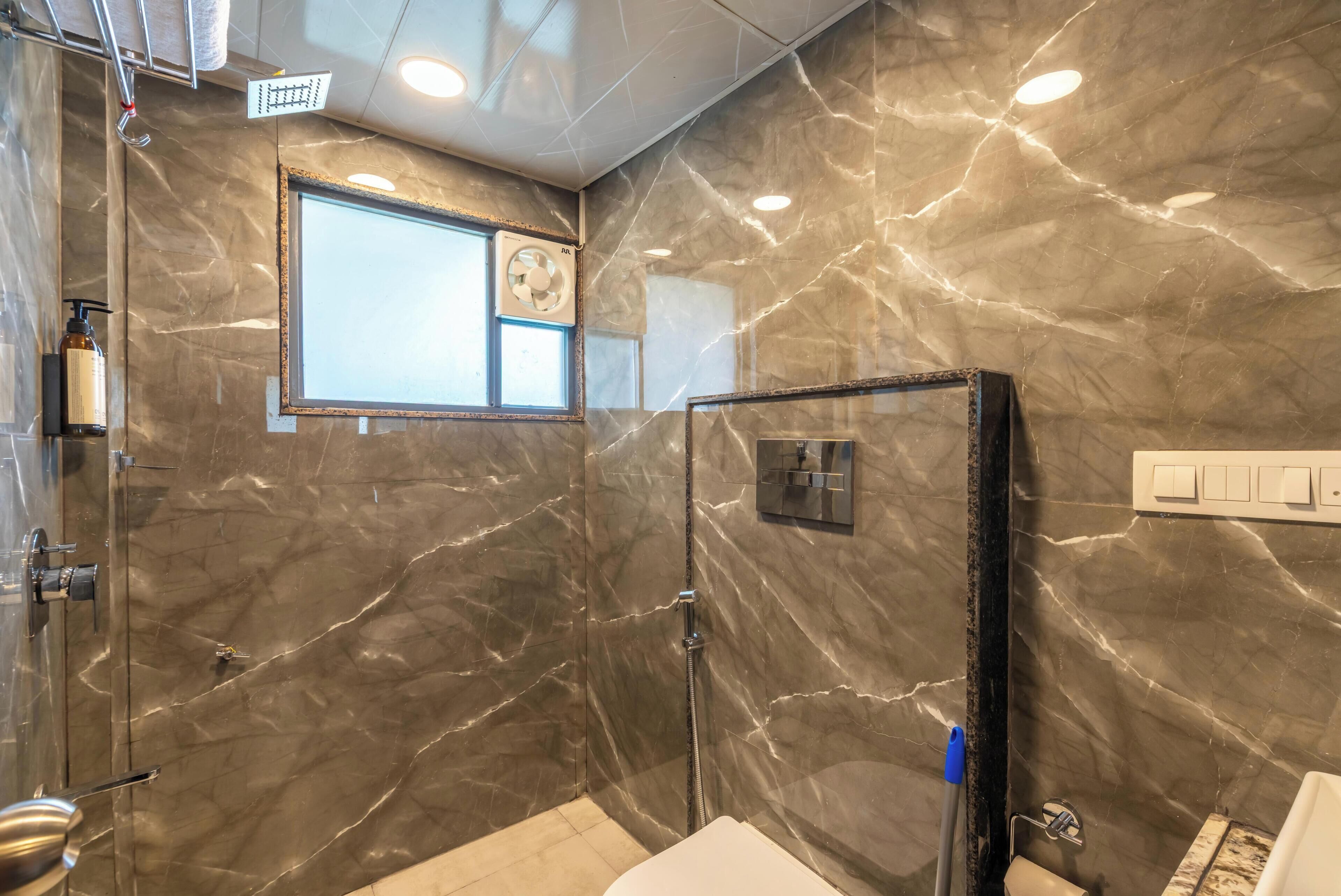 Une salle de bain moderne avec des murs en marbre, une douche en verre et une fenêtre visible.
