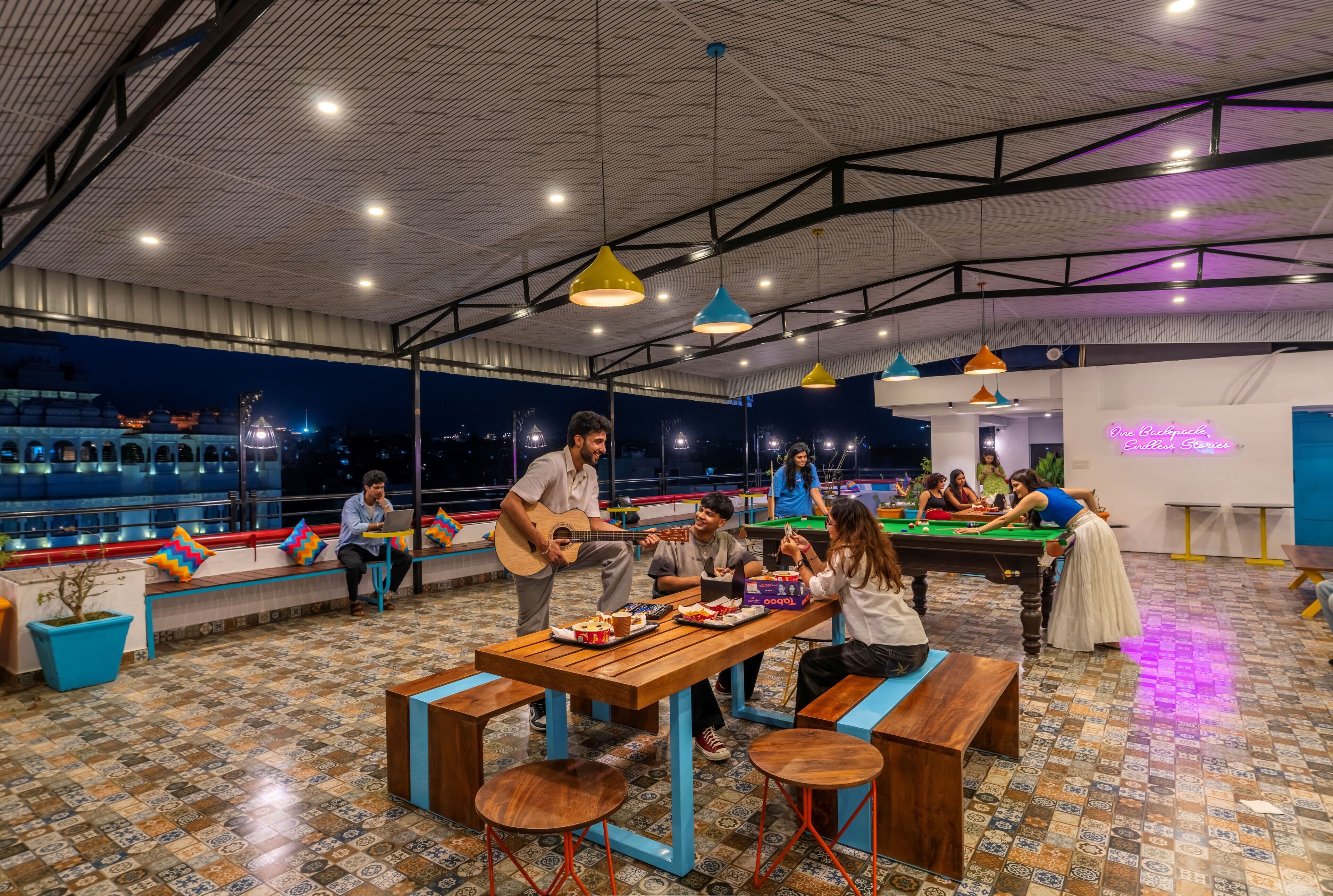 A spacious indoor area with a pool table, seating, and a person playing guitar.