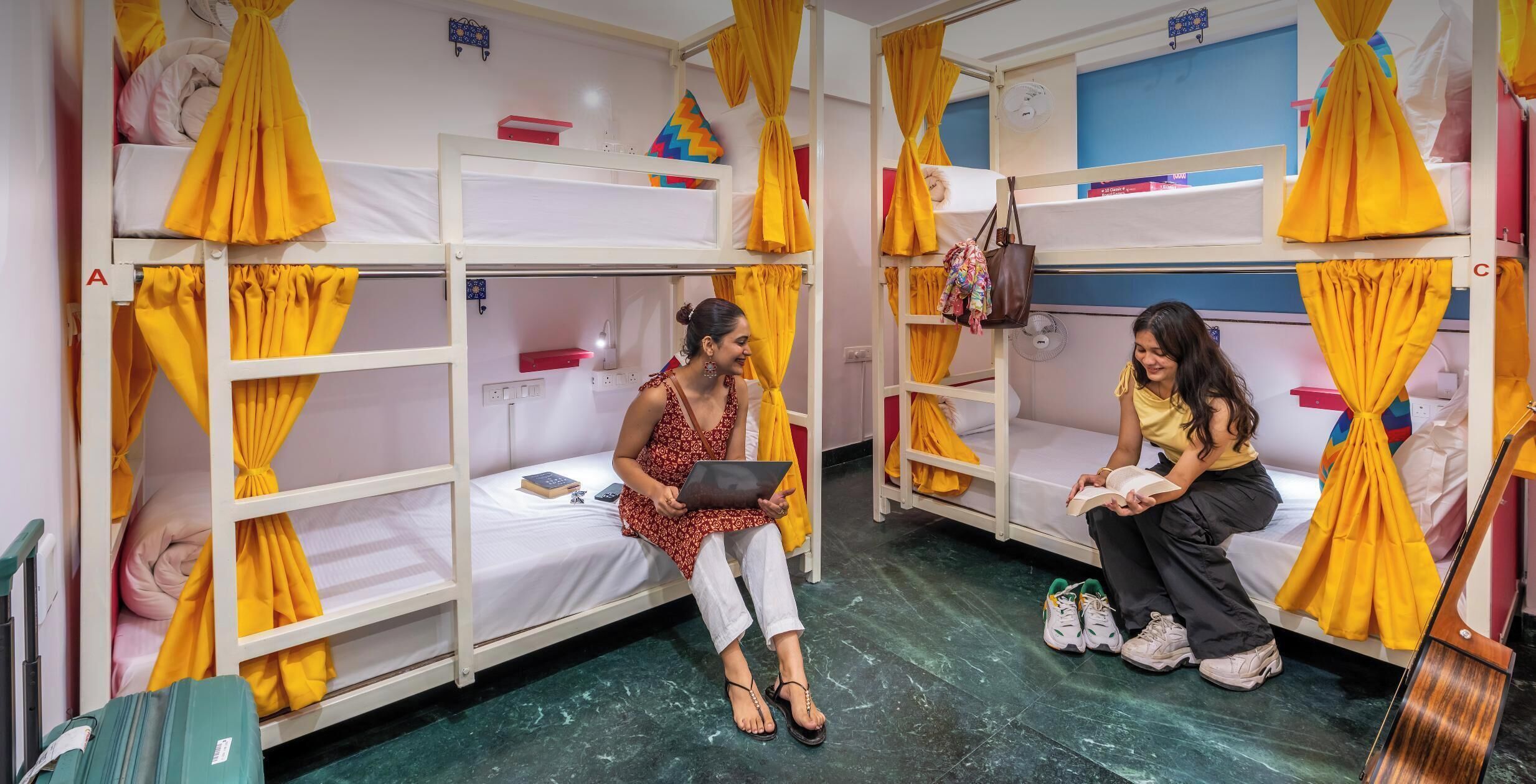 A female-only dormitory with bunk beds, yellow curtains, and a guitar.