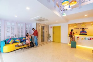 A hotel lobby with a reception desk, a yellow elevator, a blue and yellow sofa, and a staircase. - goSTOPS Plus Uadipur Gulab Bagh (Udaipur)