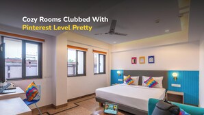 Ein Hotelzimmer mit Bett, Schreibtisch, Stuhl, Tisch und einer Couch. Es gibt Fenster, einen Deckenventilator und Wandleuchten.