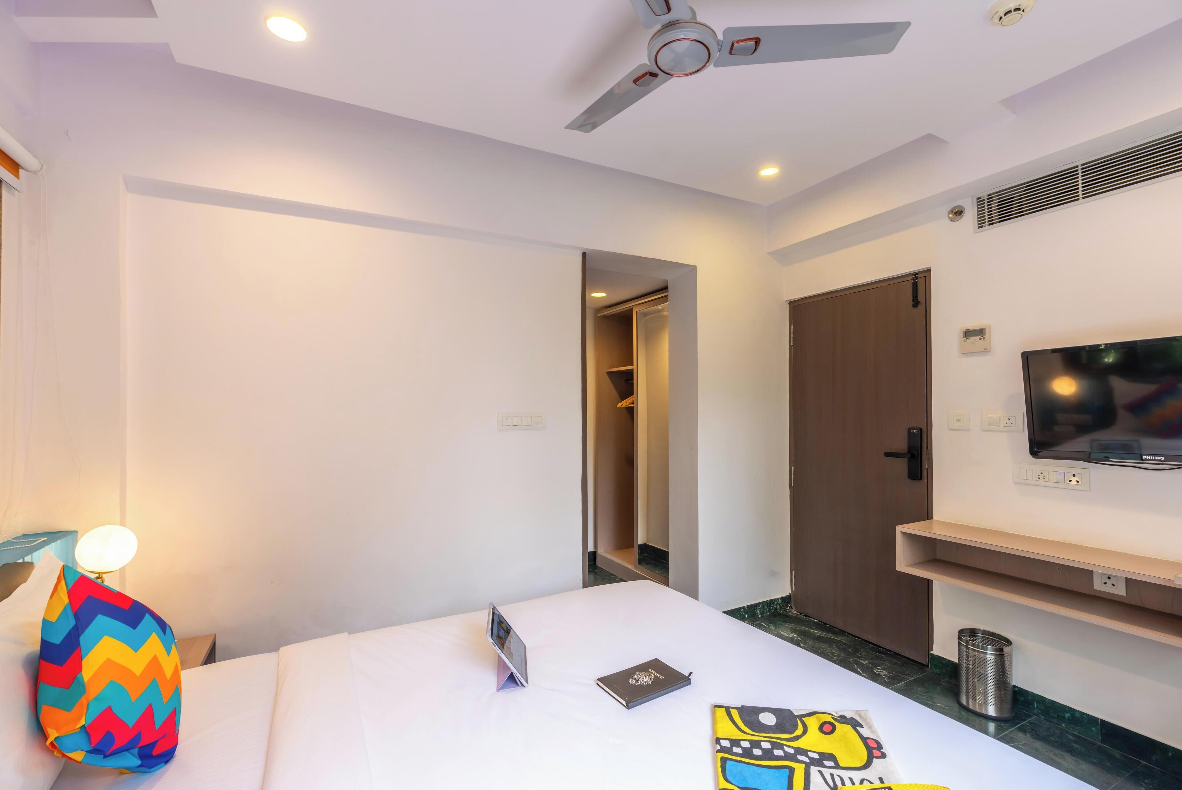 A hotel room with a bed, a TV mounted on the wall, a ceiling fan, and a walk-in closet.